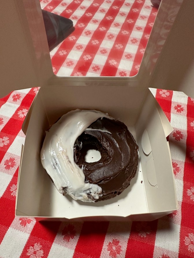 Chocolate and vanilla frosted donut in paper box.