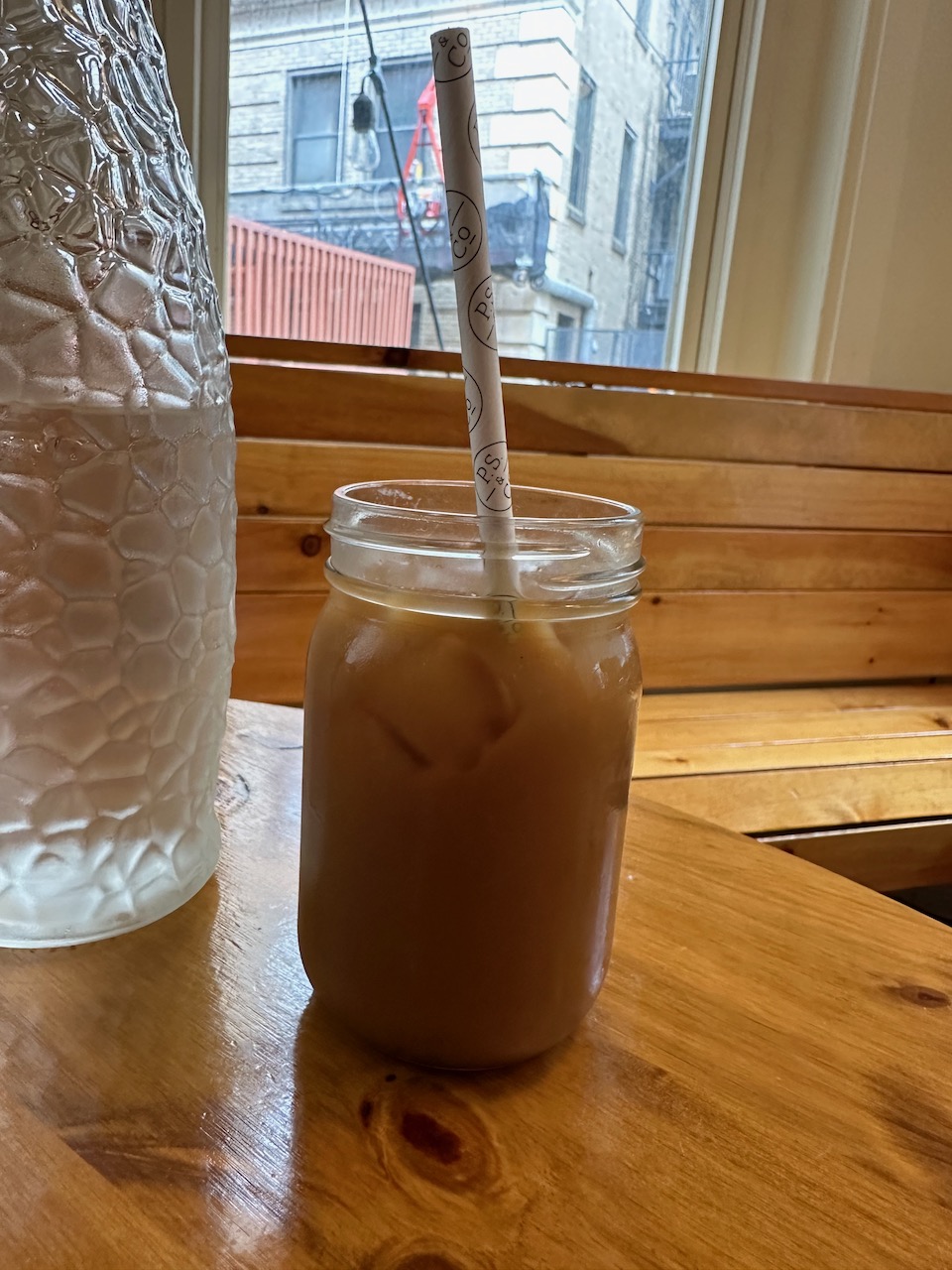 Glass mason jar holding iced coffee. The jar is on a wooden table.