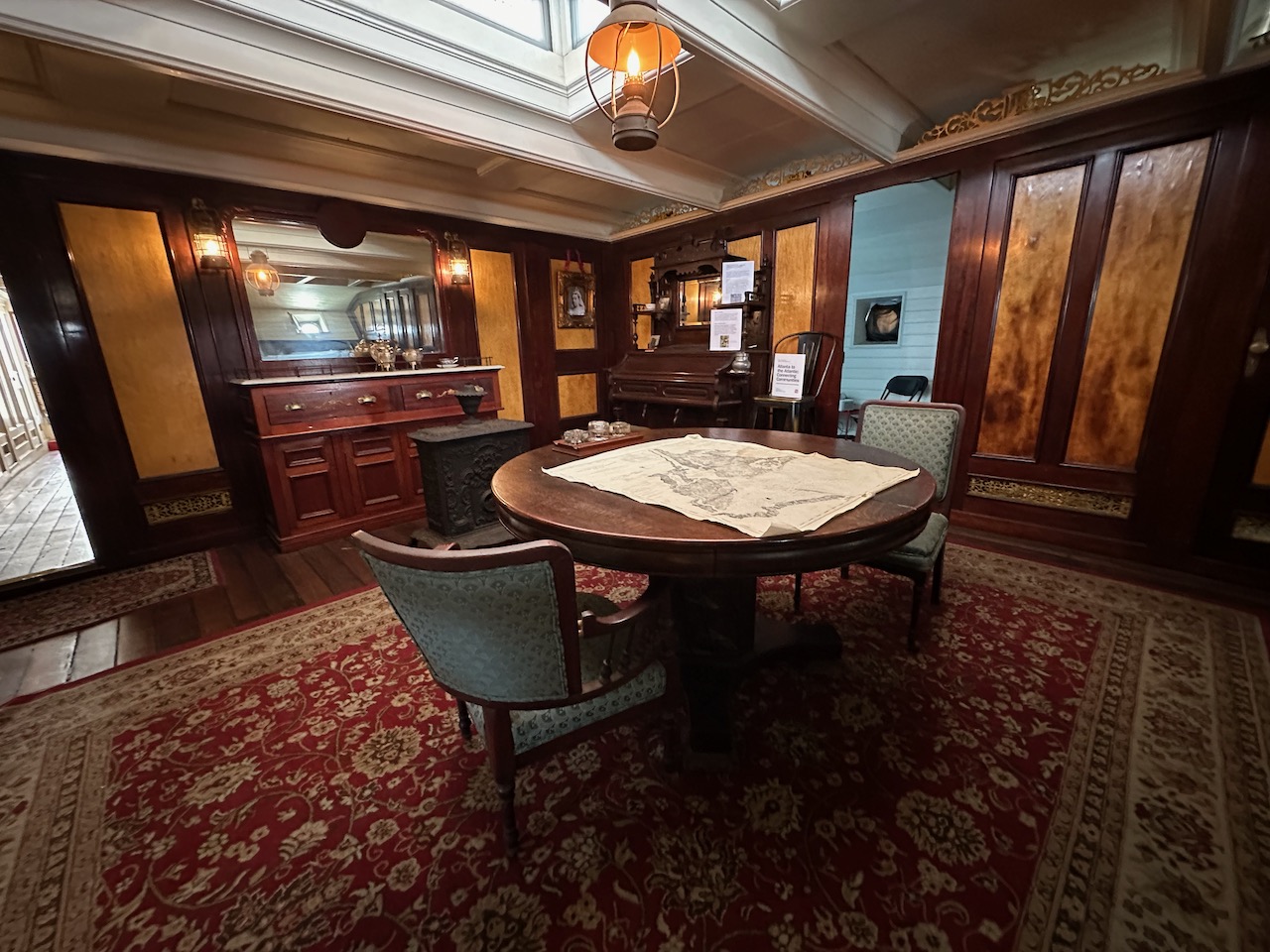 Interior of ship's saloon, with large wooden table in middle of room.