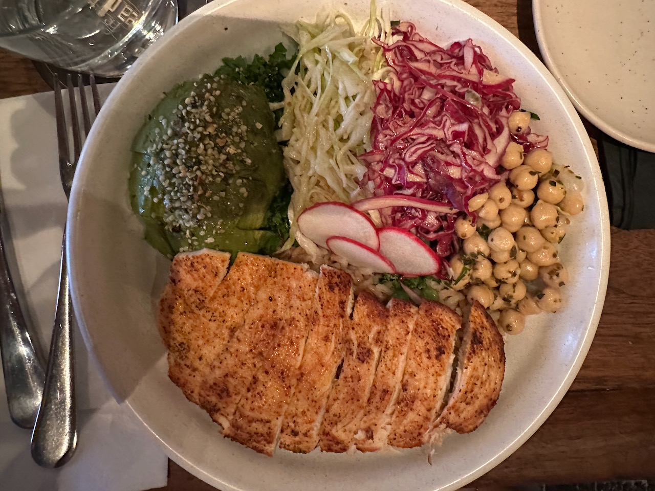 Chicken, avocado, brown rice, chickpeas, and slaw on white plate.