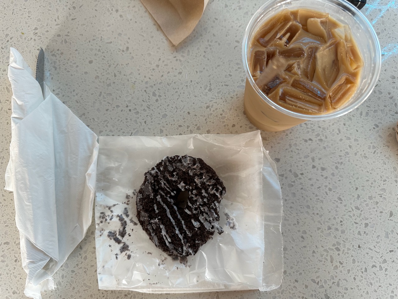 Iced oat milk latte and chocolate donut on white table.