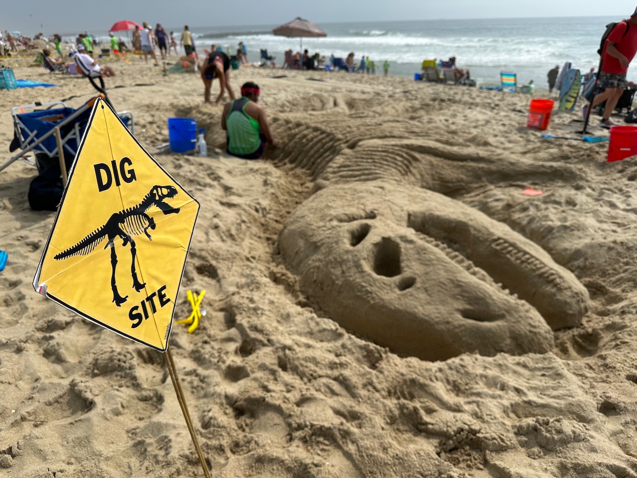 Sand skeleton of Tyrannosaurus Rex, with yellow sign beside it that reads DIG SITE.