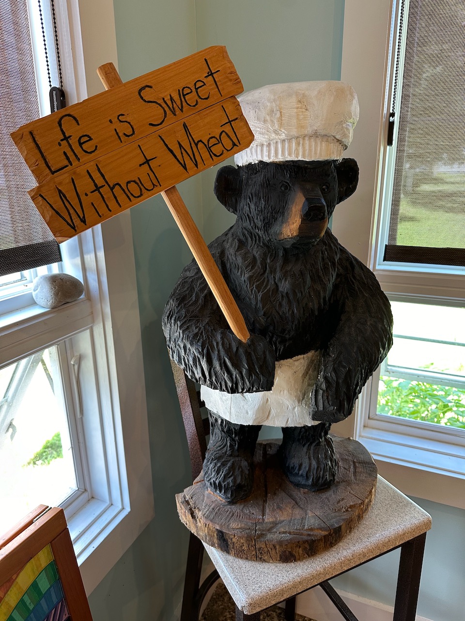 Statue of bear, wearing chef's hat and apron, holding sign that reads LIFE IS SWEET WITHOUT WHEAT.