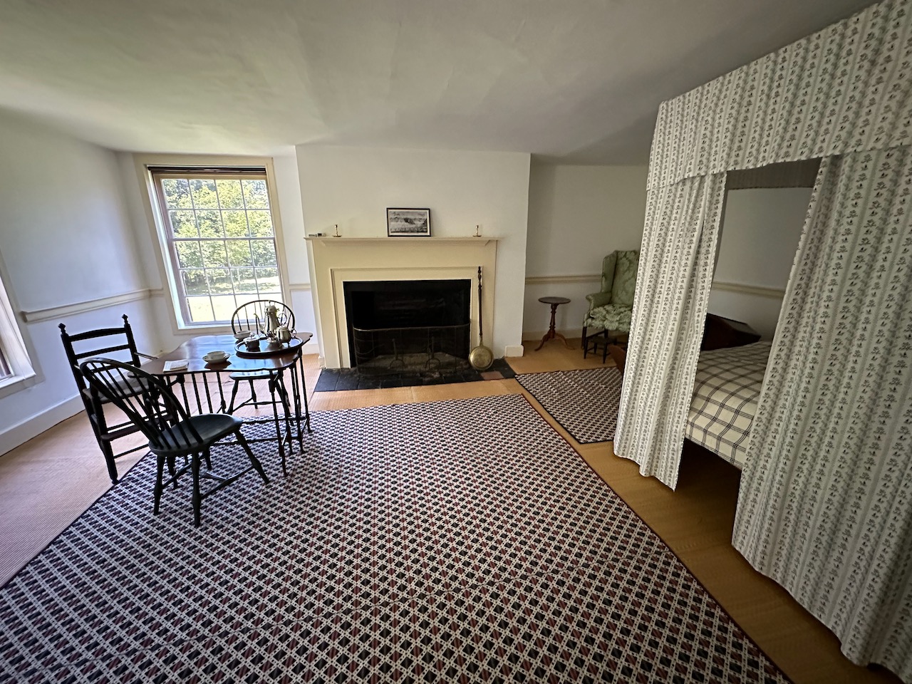 Master bedroom of Schuyler House, including table with two seats, fire place, and four poster bed.