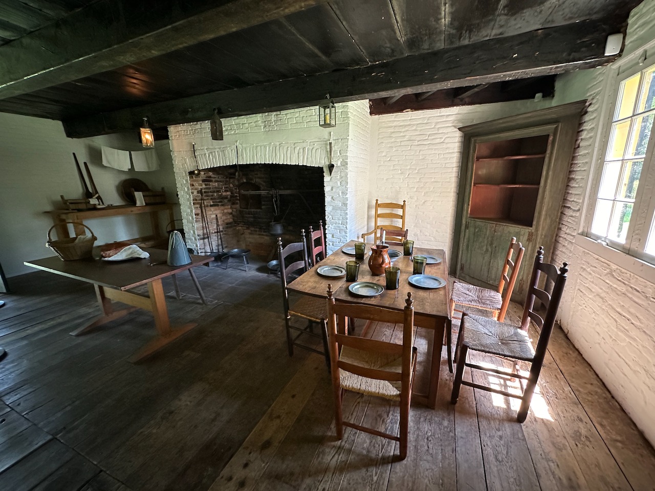 Kitchen, with large brick hearth, and a simple wooden table with six chairs surrounding it.