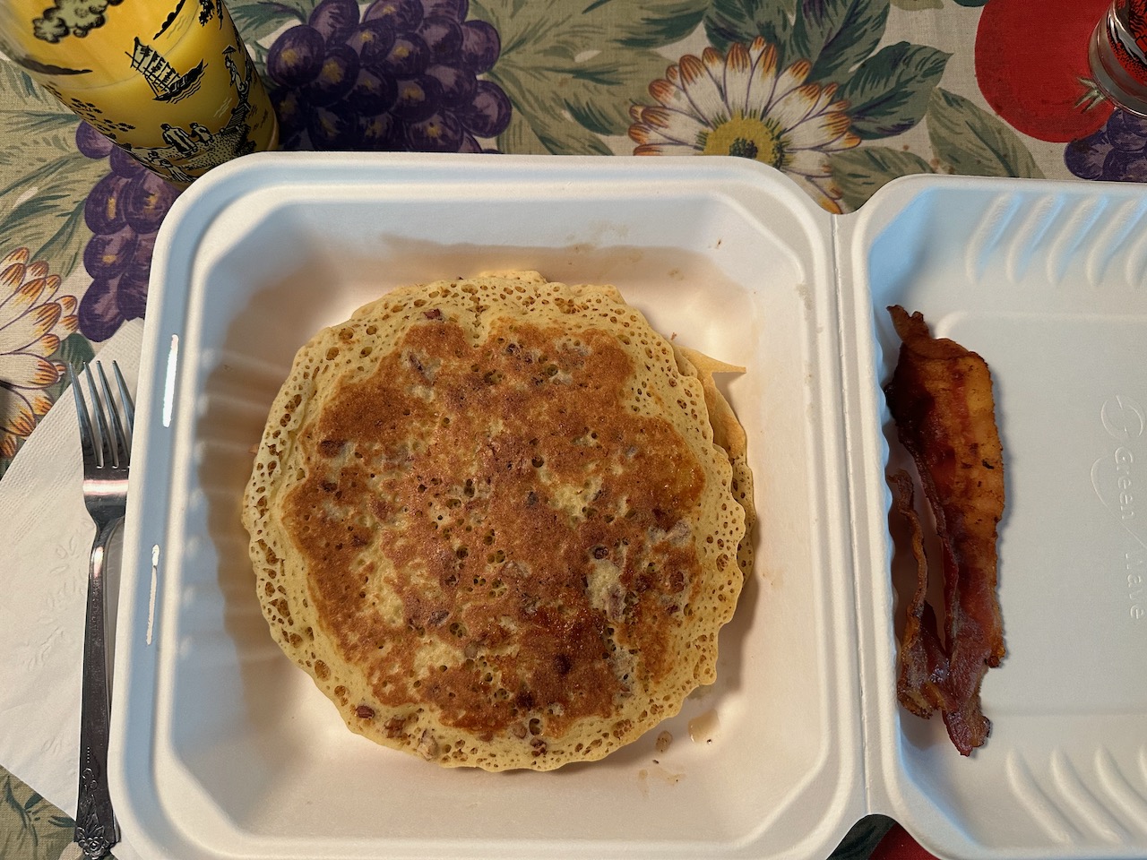 Pancakes and bacon in styrofoam takeout container.