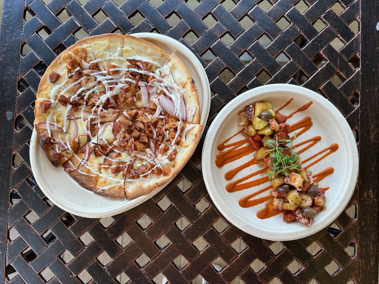 Two plates on metal table. One has a flatbread pizza, the other has grilled octopus.