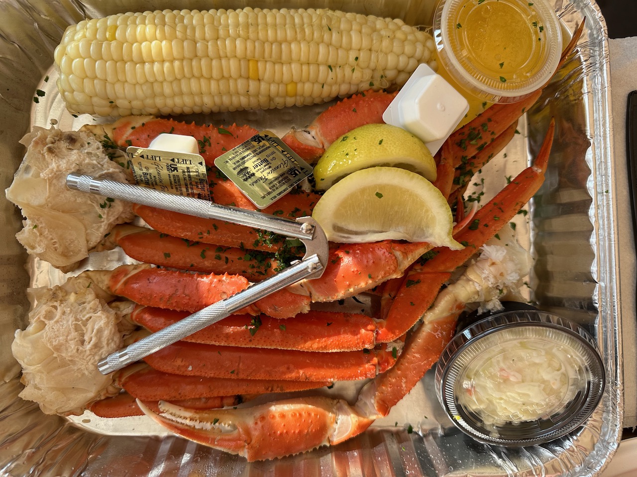 Tin foil plate with corn and snow crab legs.
