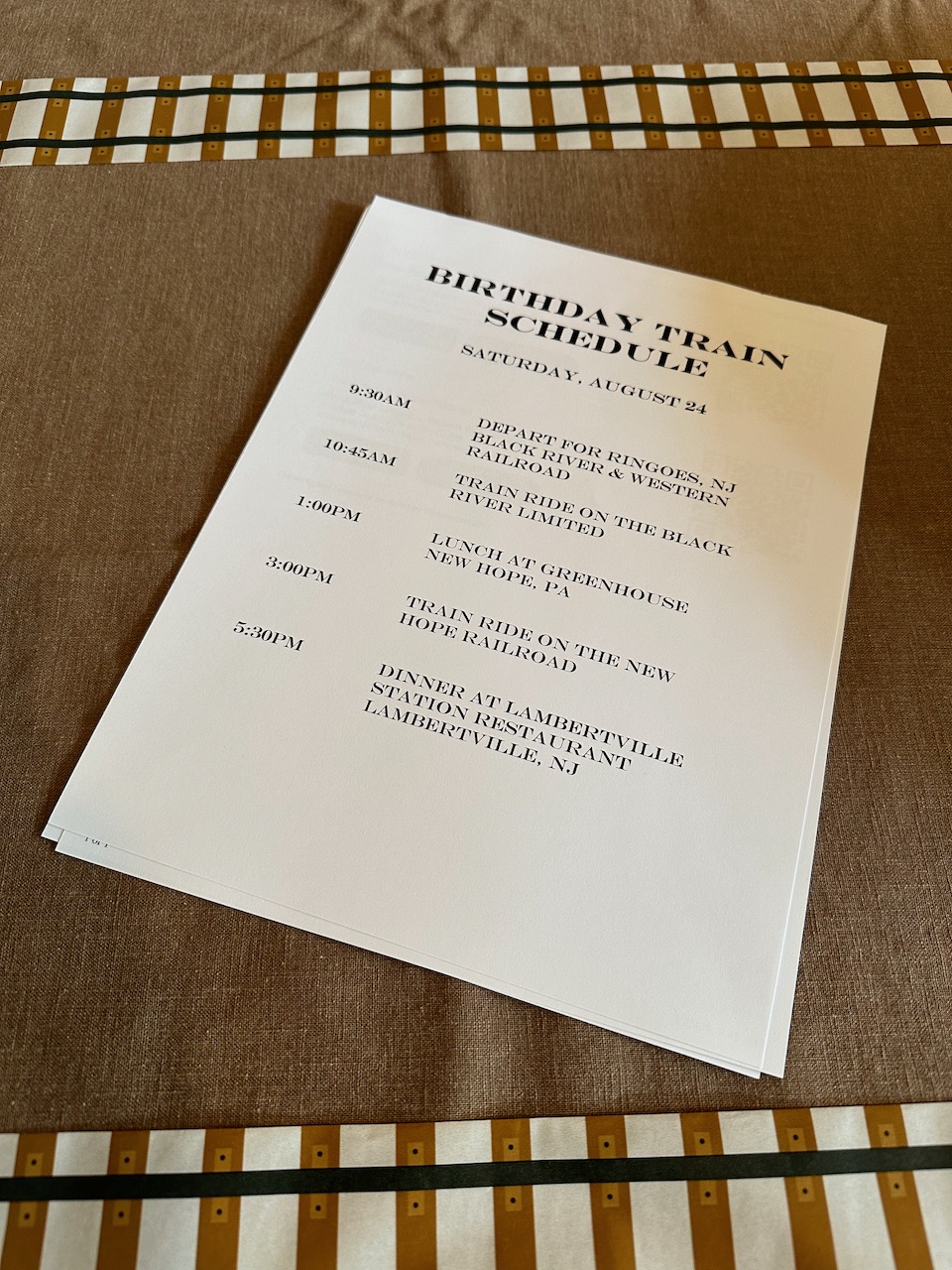 Printed schedule for birthday road trip on white paper. Paper is on a tablecloth that is decorated with train track ribbons.