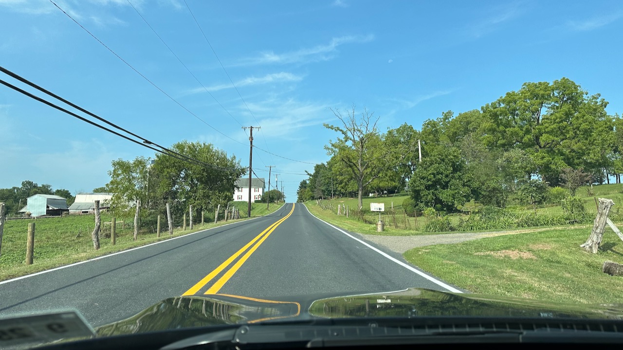 View of two-lane road with farm on left side of road.
