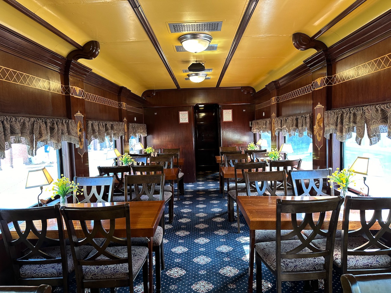 Interior of dining car, with wooden tables on both sides of aisle.