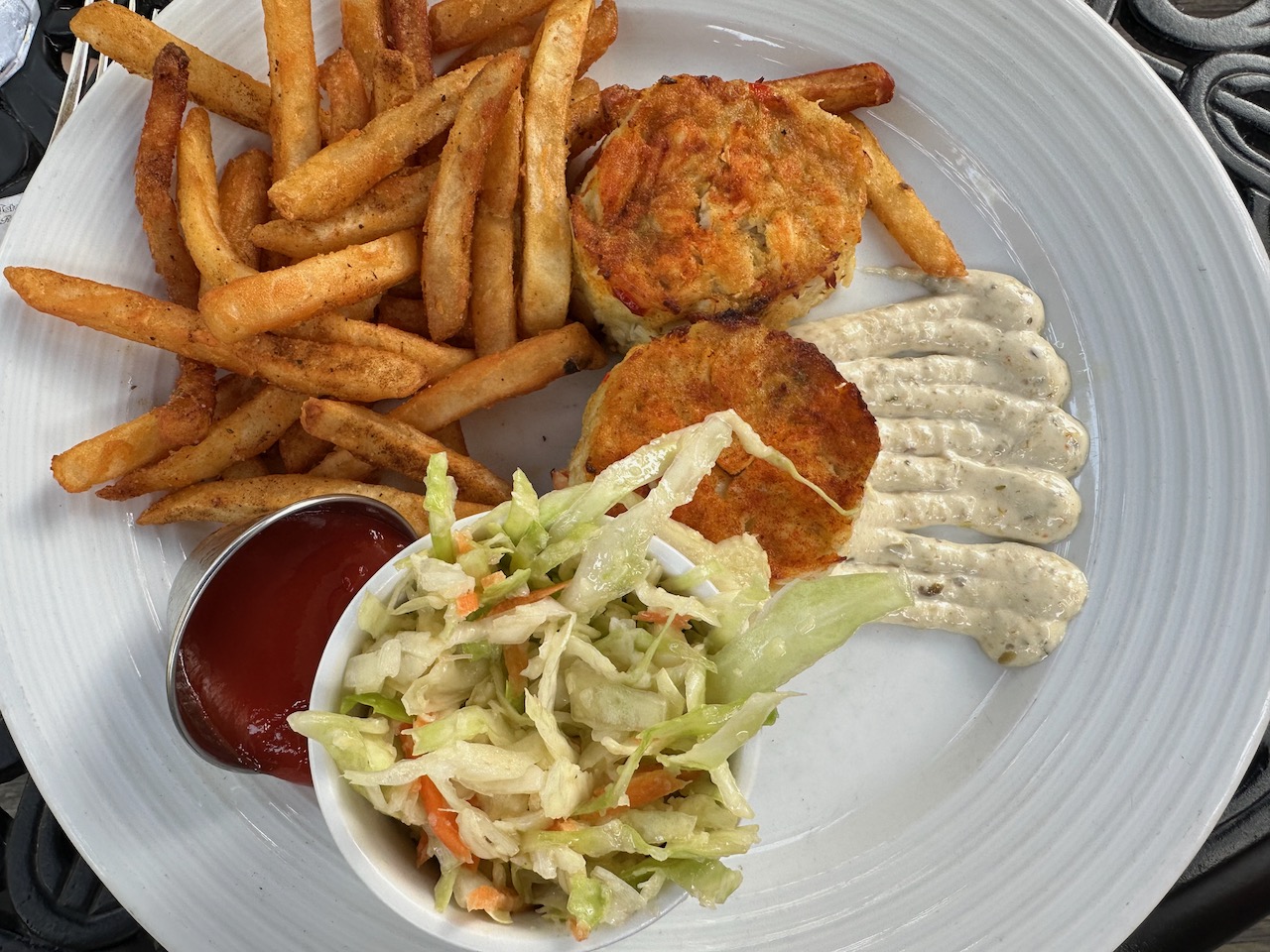 Crab cakes, coleslaw, and fries on white plate.