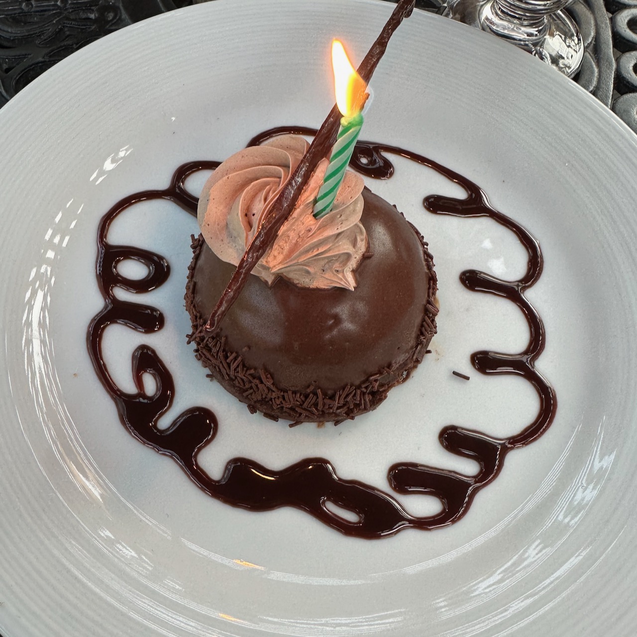 Flourless birthday cake on plate, with burning candle in cake.