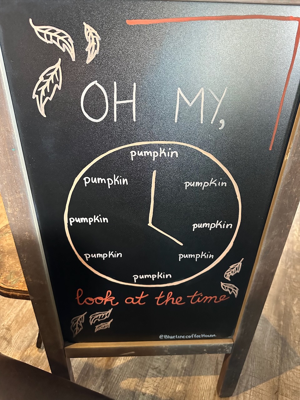 Chalkboard sign with hand-drawn clock and every time on clock face is the word 