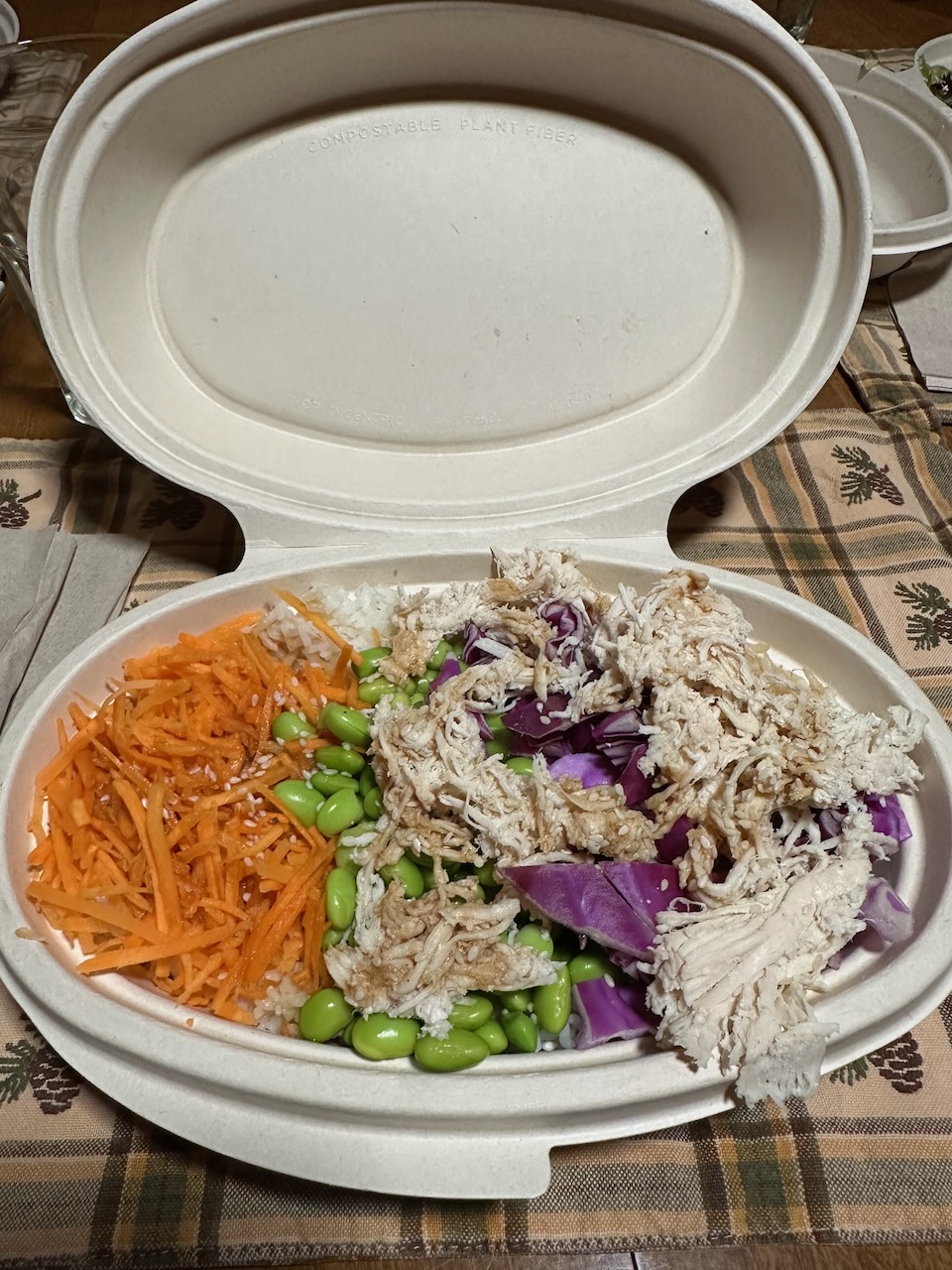 Chicken, edamame, carrots, cabbage and rice in white paper bowl on table.