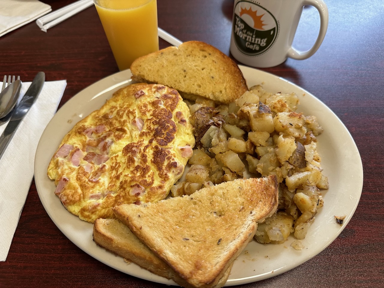 Ham omelette with potatoes and toast on white plate.