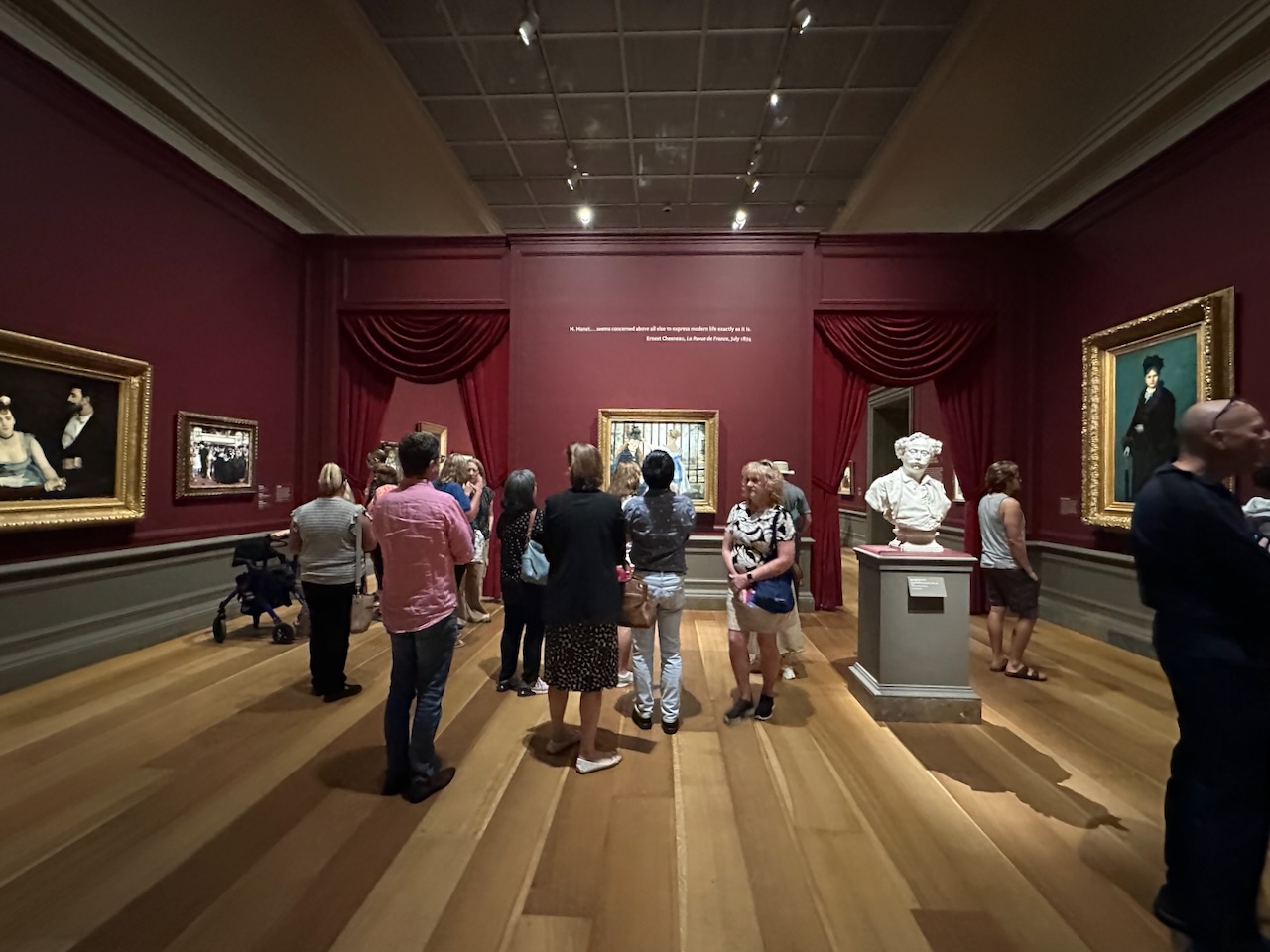 Gallery filled with Impressionist artwork, and a crowd of approximately 20 people milling about gallery.