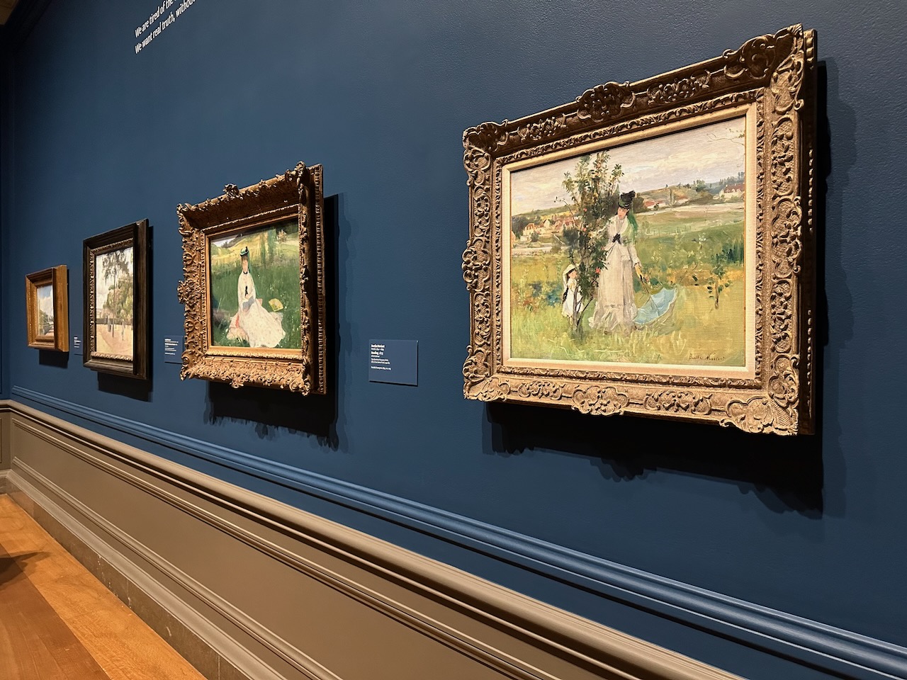 Four impressionist paintings on wall of gallery.