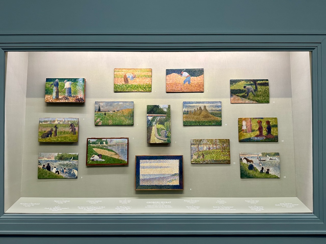 Fourteen sketches of paintings by artist George Seurat, hanging in gallery.