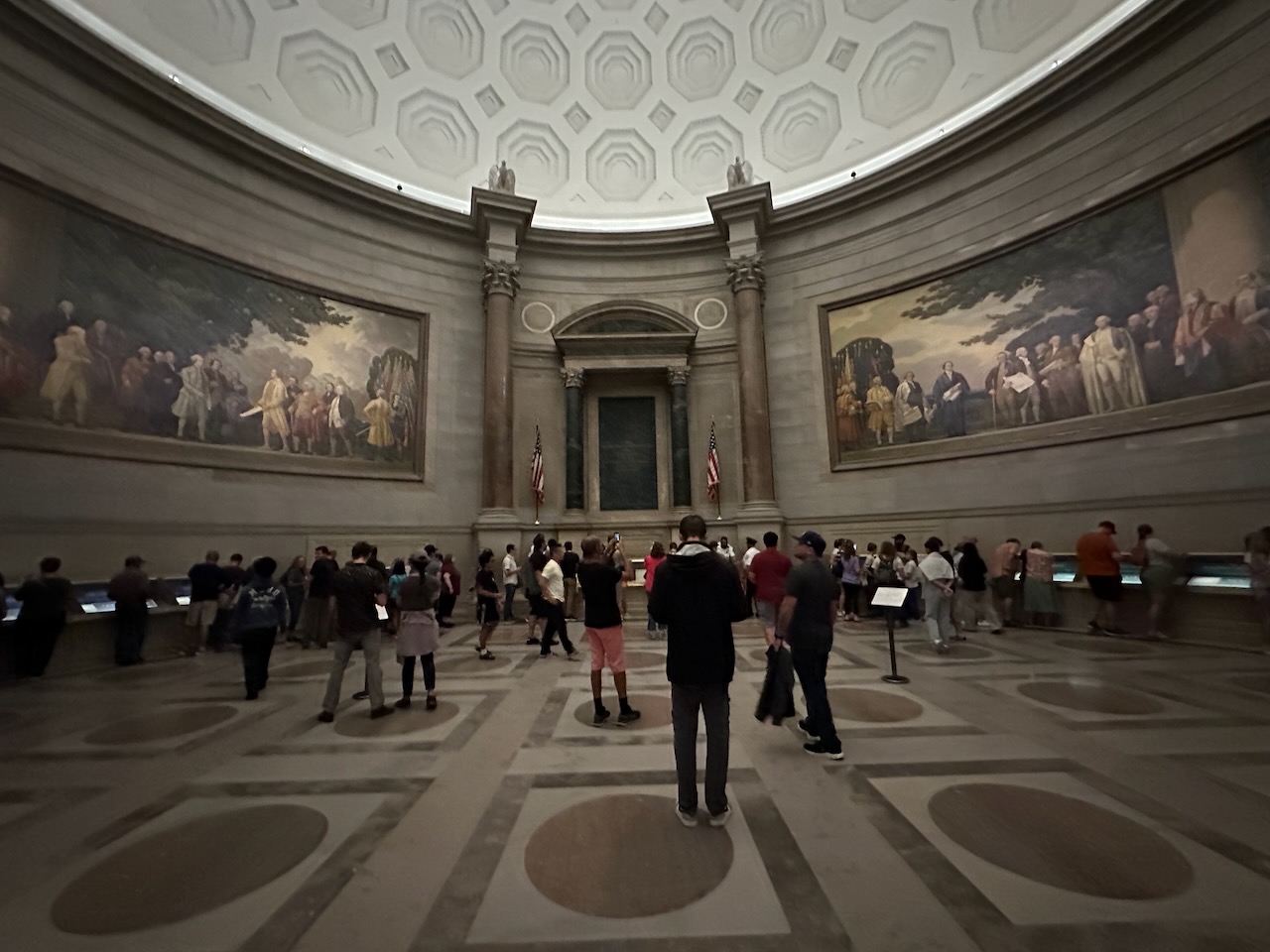 Interior of rotunda of national archives, with crowd of people looking at exhibits near walls.