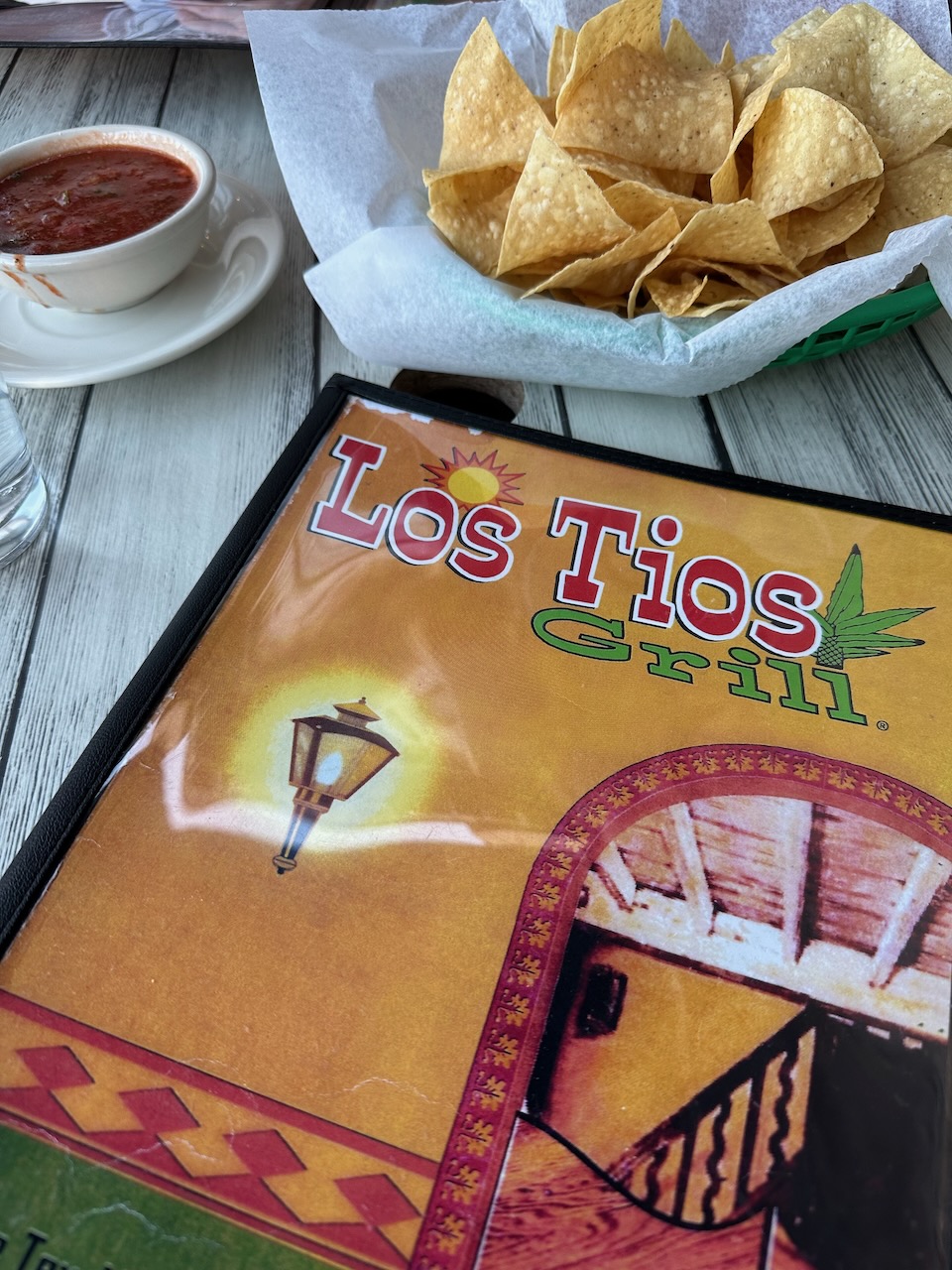 Menu on table, with basket of chips and bowl of salsa in background.