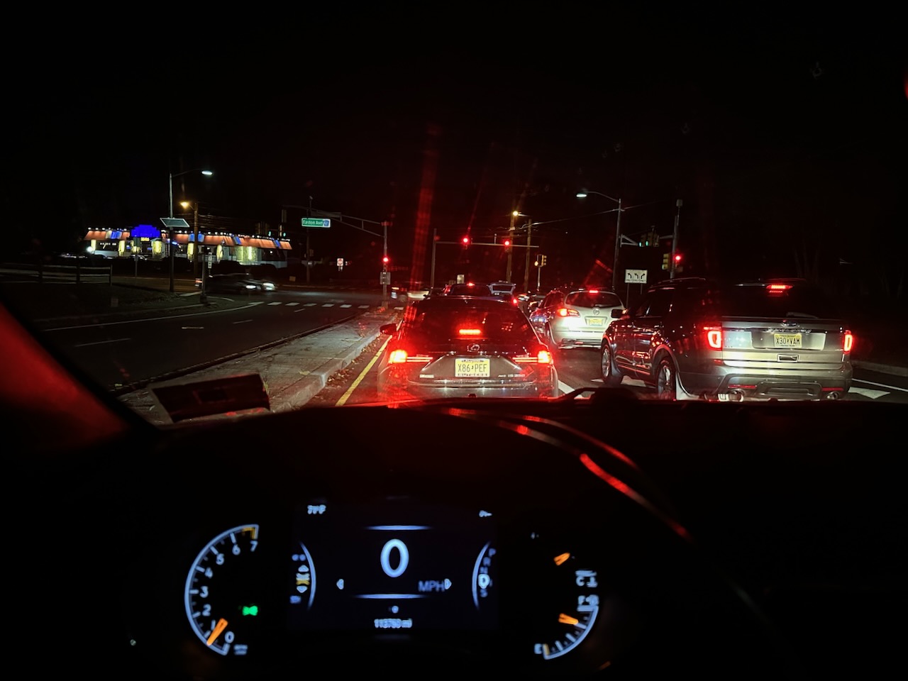 View of road at night behind wheel of 2014 Jeep Grand Cherokee. There is traffic at a stoplight ahead of the vehicle.