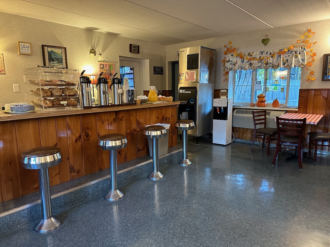 Interior of Coffee Shop at Roosevelt Inn, with a counter and stools on the left side of the image, a window in the rear, and a small table in the background.