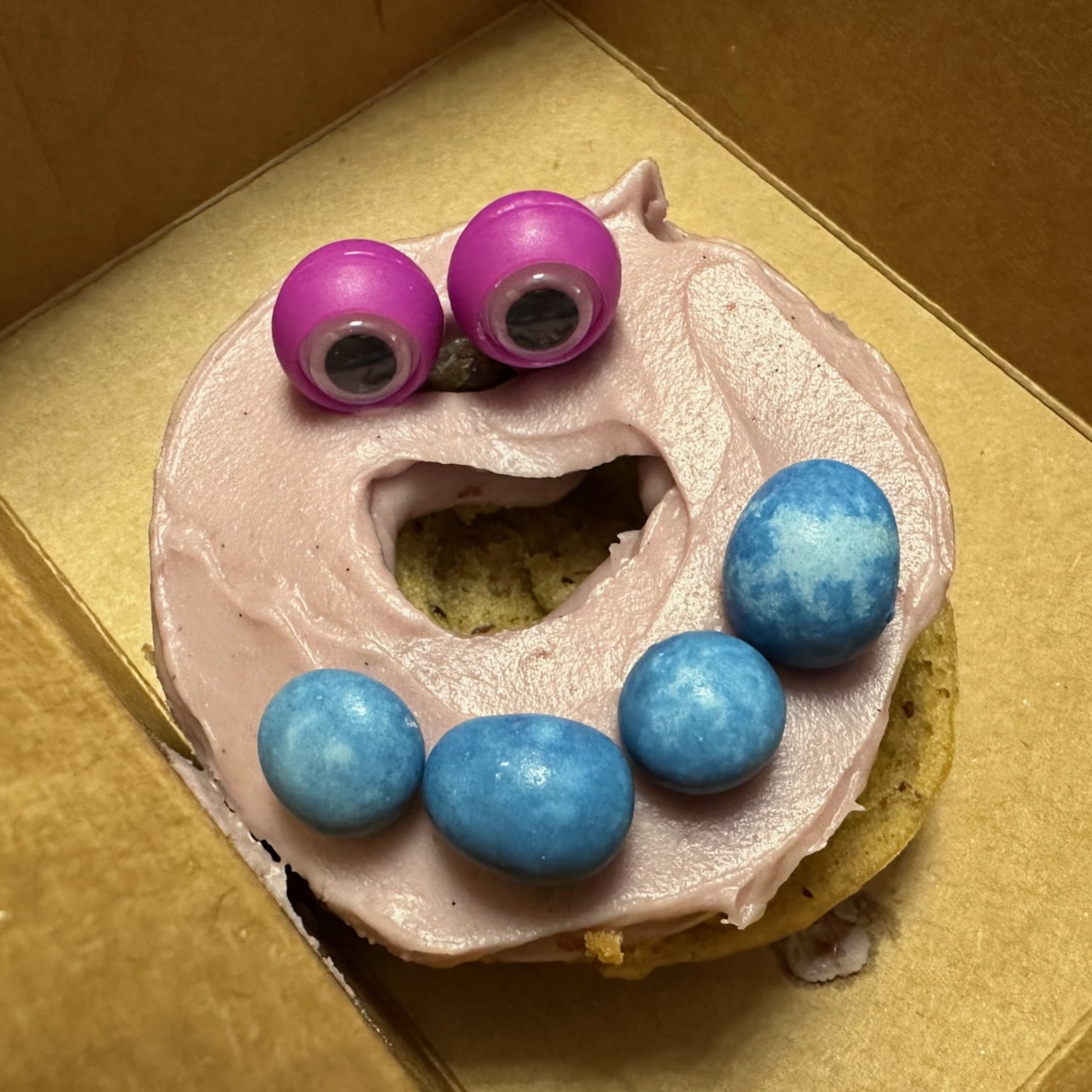 Donut covered in icing with googley eyes.