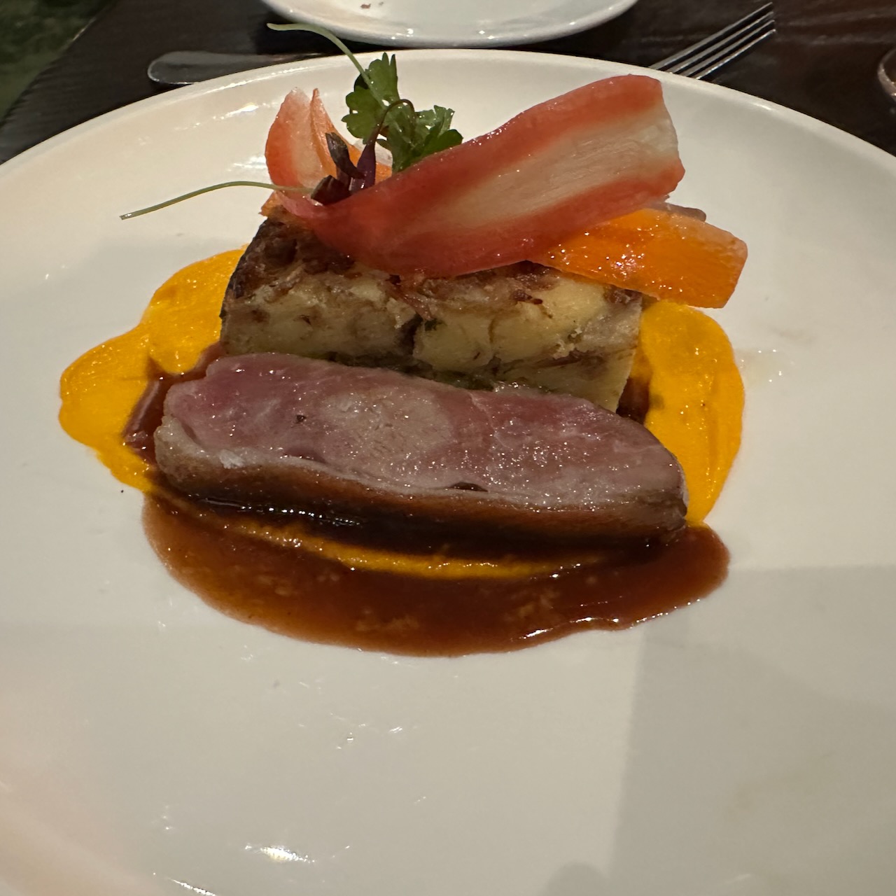 Duck breast and bread pudding on white plate.