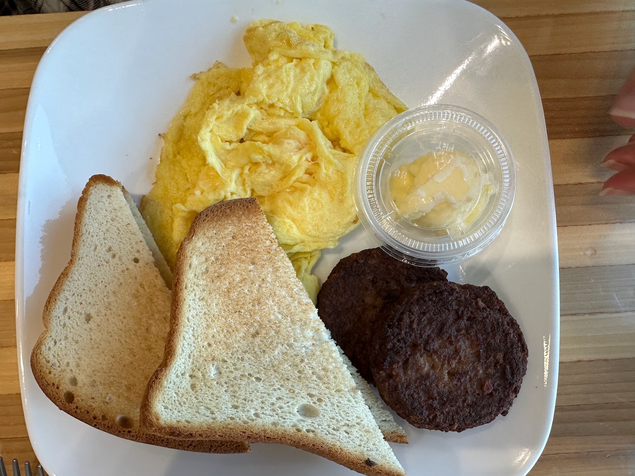 Eggs, vegetarian sausage, and toast on white plate.