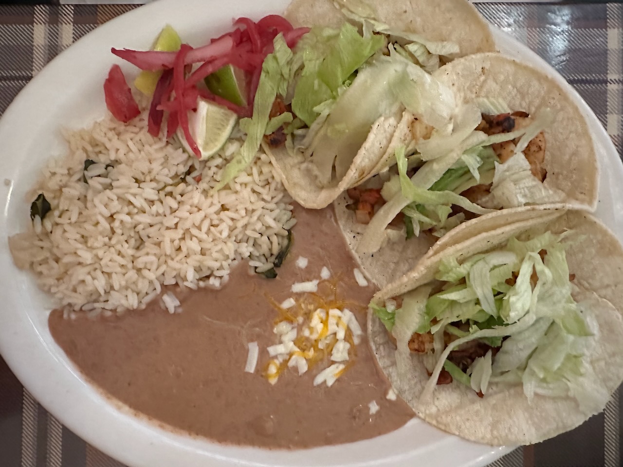Tacos, refried beans, and tortillas on white plate.