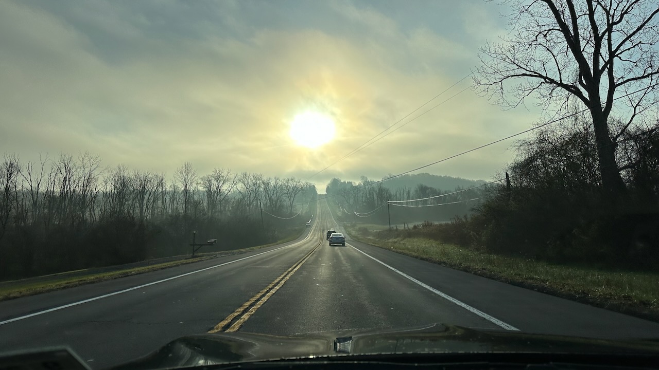 View of US-20 with rising sun and fog over roadway.