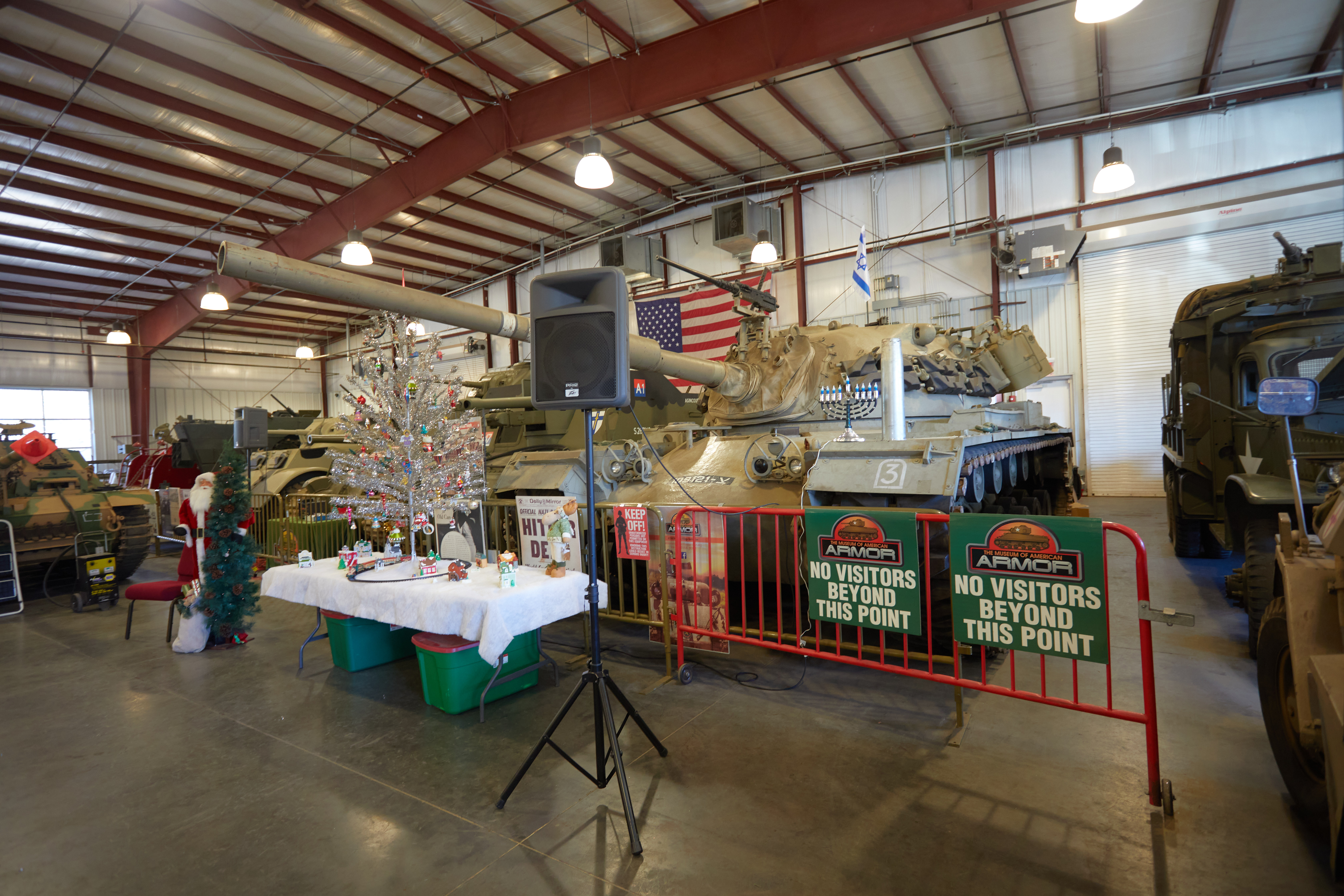 M48 tank with menorah on top of it. On a table in from to frank is a Christmas Tree and model train set.
