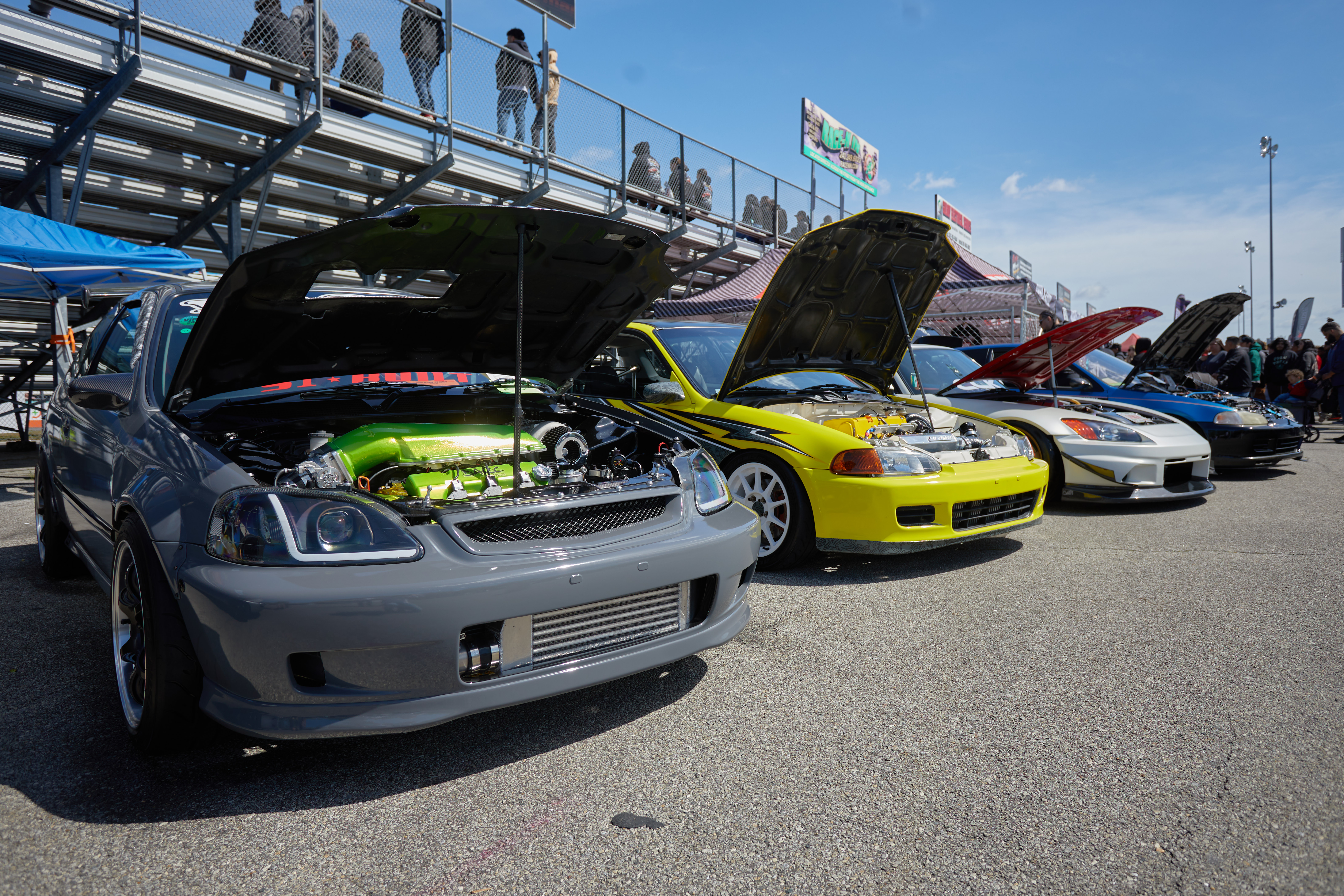 Three modified Honda Civics and a Honda S2000, lined up behind grandstands.