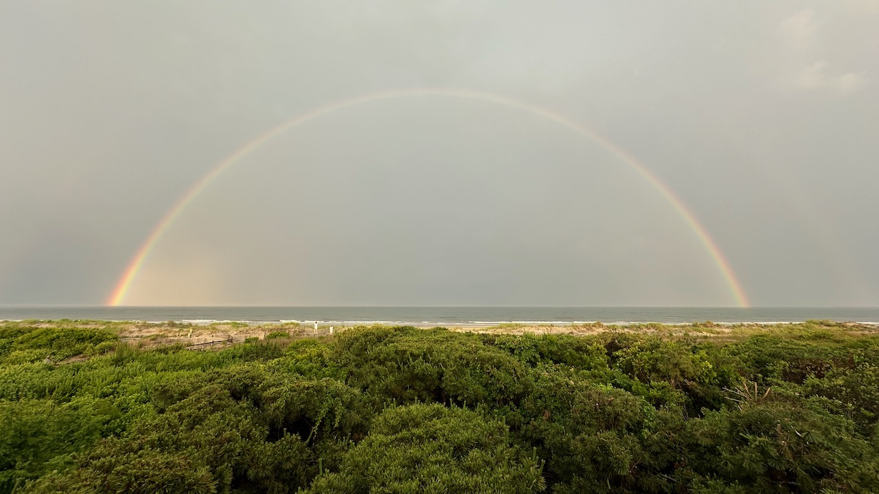 Rainbow spreading over beach, with gray skies in background.