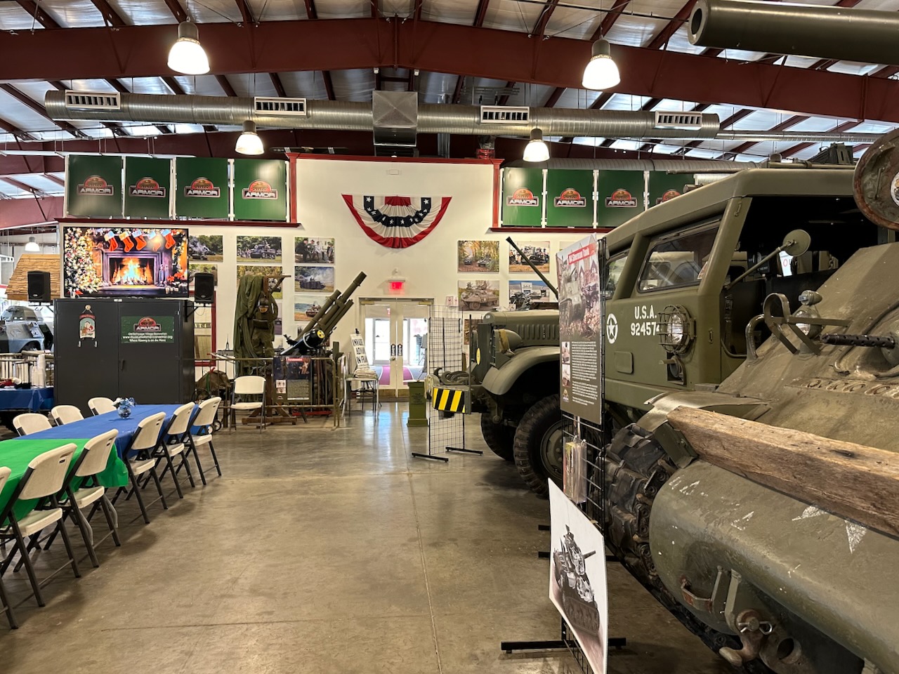 Interior of museum, with military vehicles on right and folding tables with chairs on left.