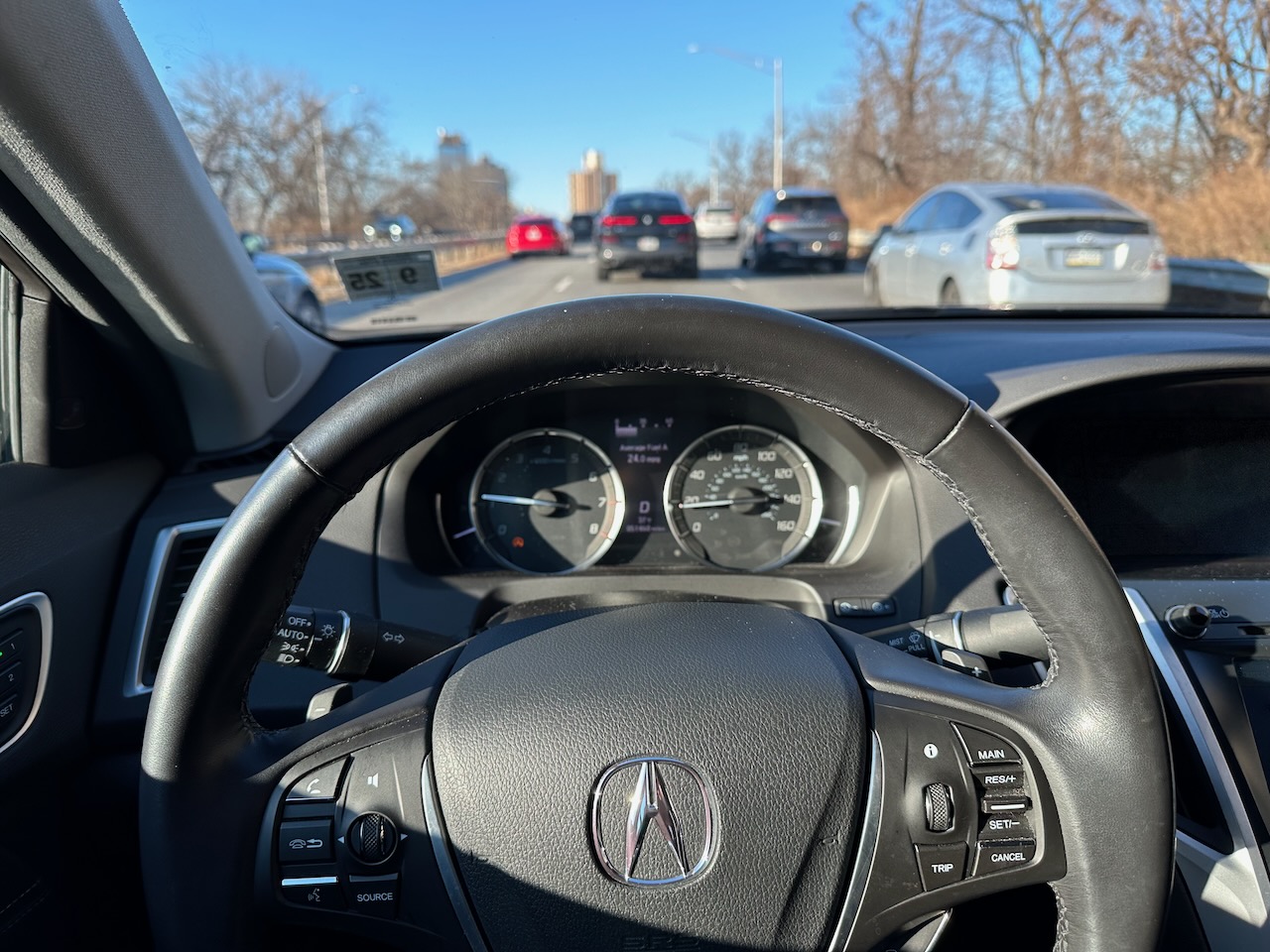 View of Acura TLX steering wheel and dashboard, with traffic in background.
