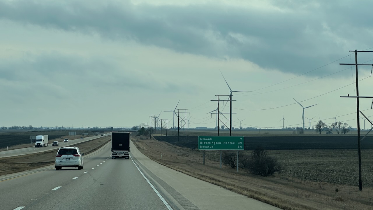 Interstate 39 in Illinois, with roadside sign that lists distances to Minonk, Bloomington, and Decatur. Windmills are in a field to the right of the highway.