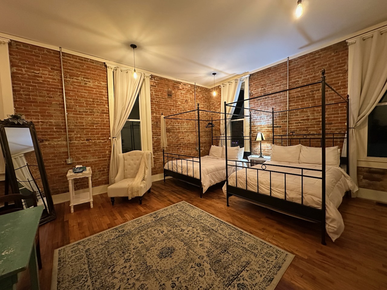 Room at The Eighteen-Ninety Sleepover hotel in Casey. The walls are exposed brick, and there are two queen-size four-poster beds in room.