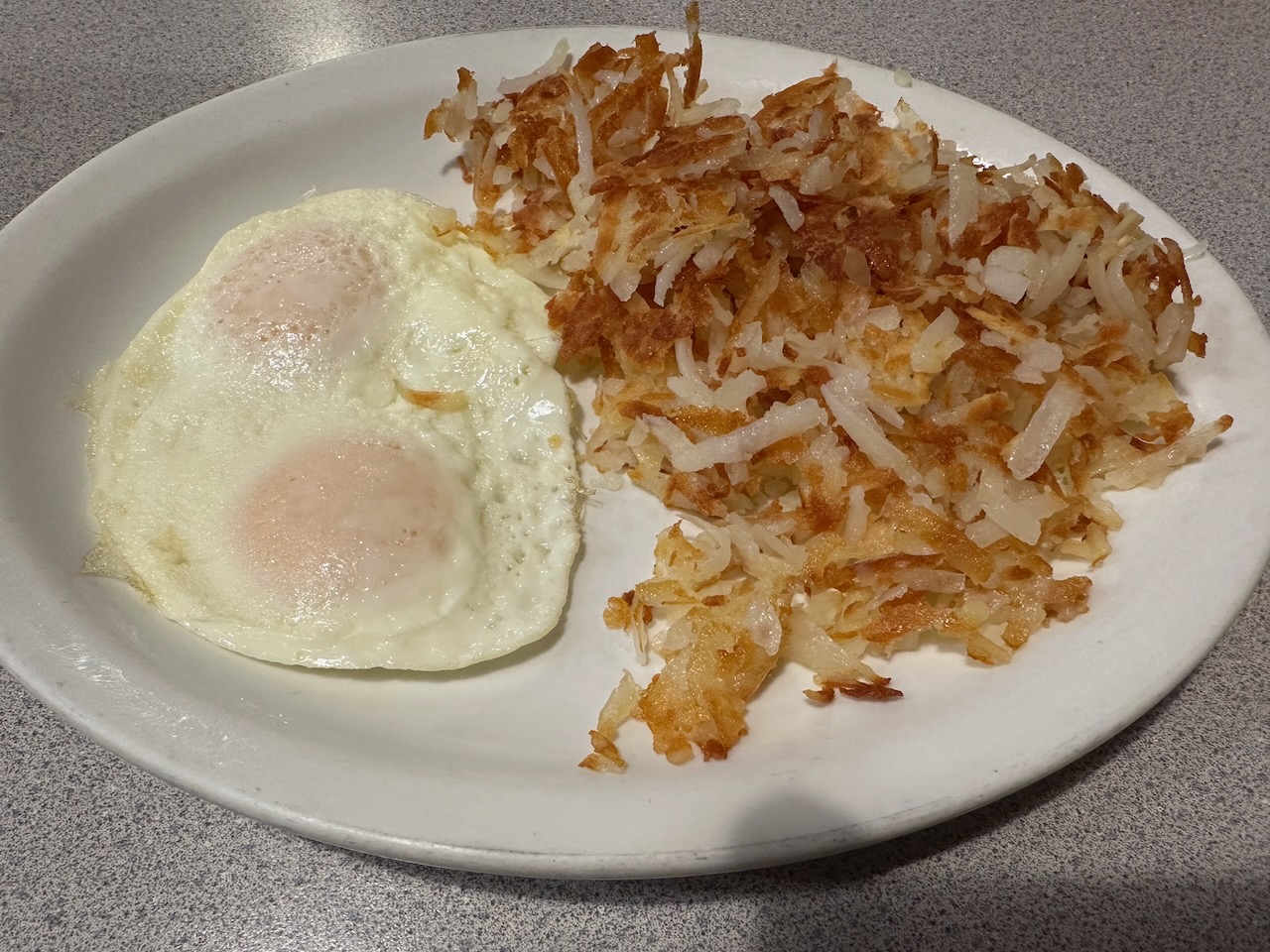 Eggs over easy with side of home fries on white plate.