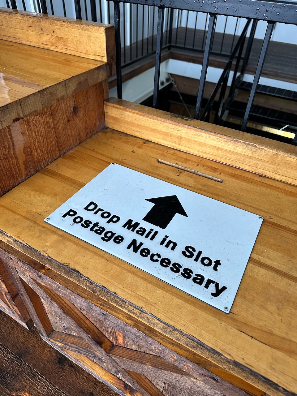 Wooden box with sign that says DROP MAIL IN SLOT POSTAGE NECESSARY.