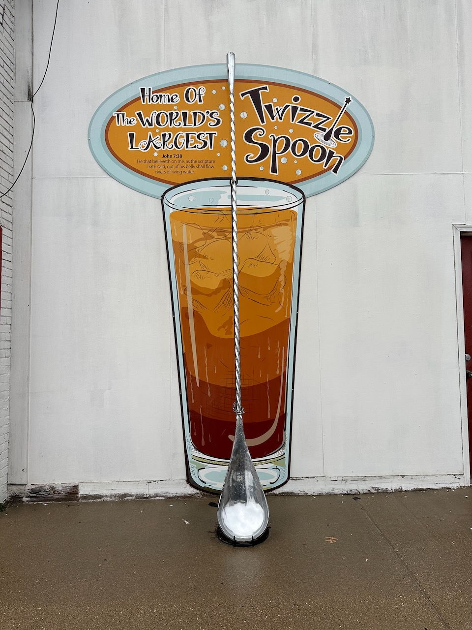 Mural of beverage on side of building with World's Largest Swizzle Spoon in foreground.