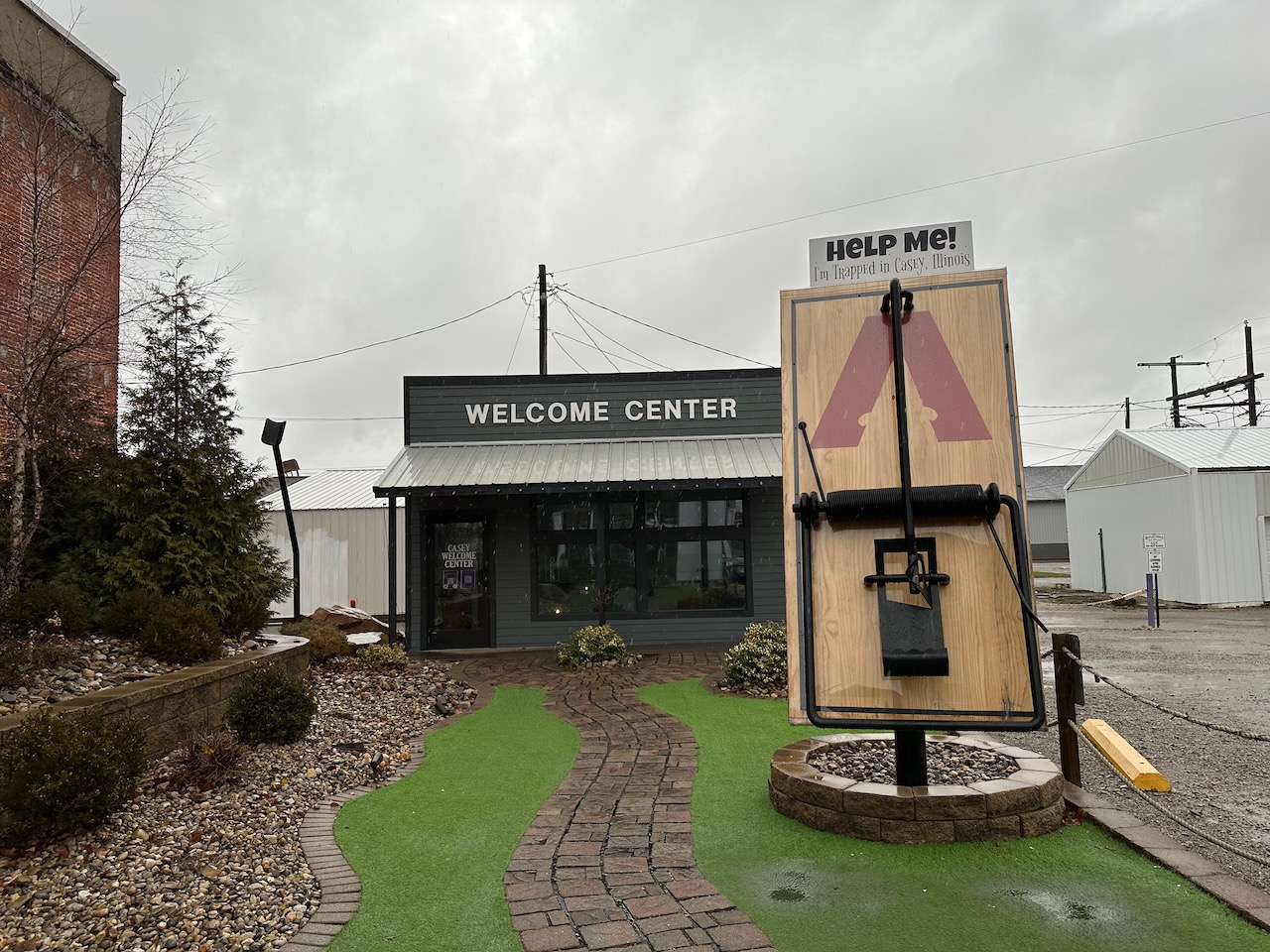 Large mousetrap with sign that says HELP ME I'M TRAPPED IN CASE ILLINOIS next to Casey Welcome Center.