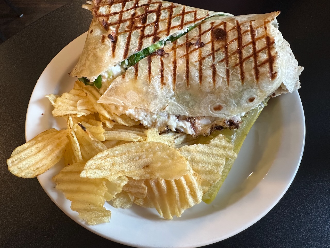 Chicken salad wrap with side of potato chips on white plate.