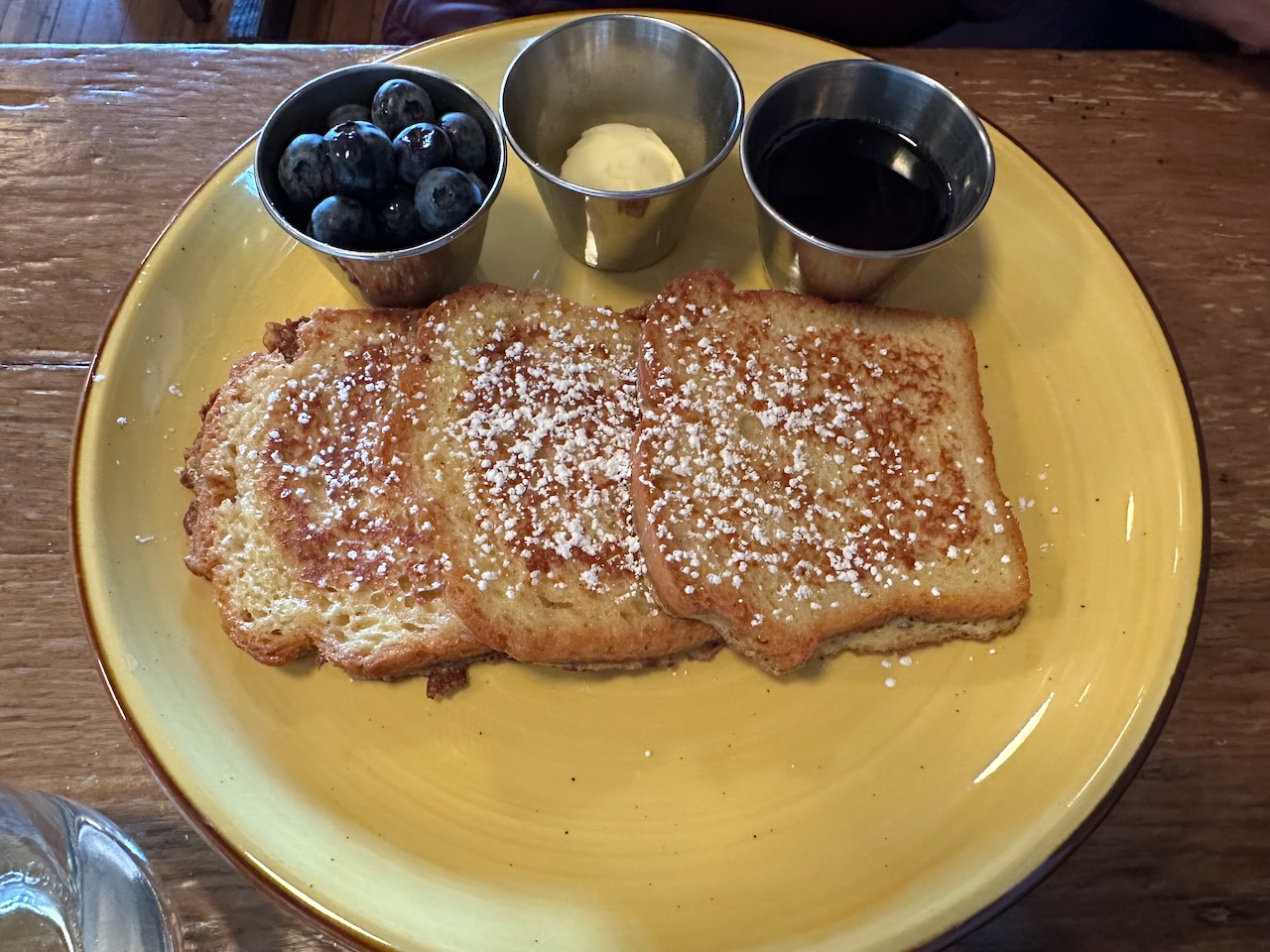 French toast on plate, with sides of butter, blueberries, and maple syrup. 