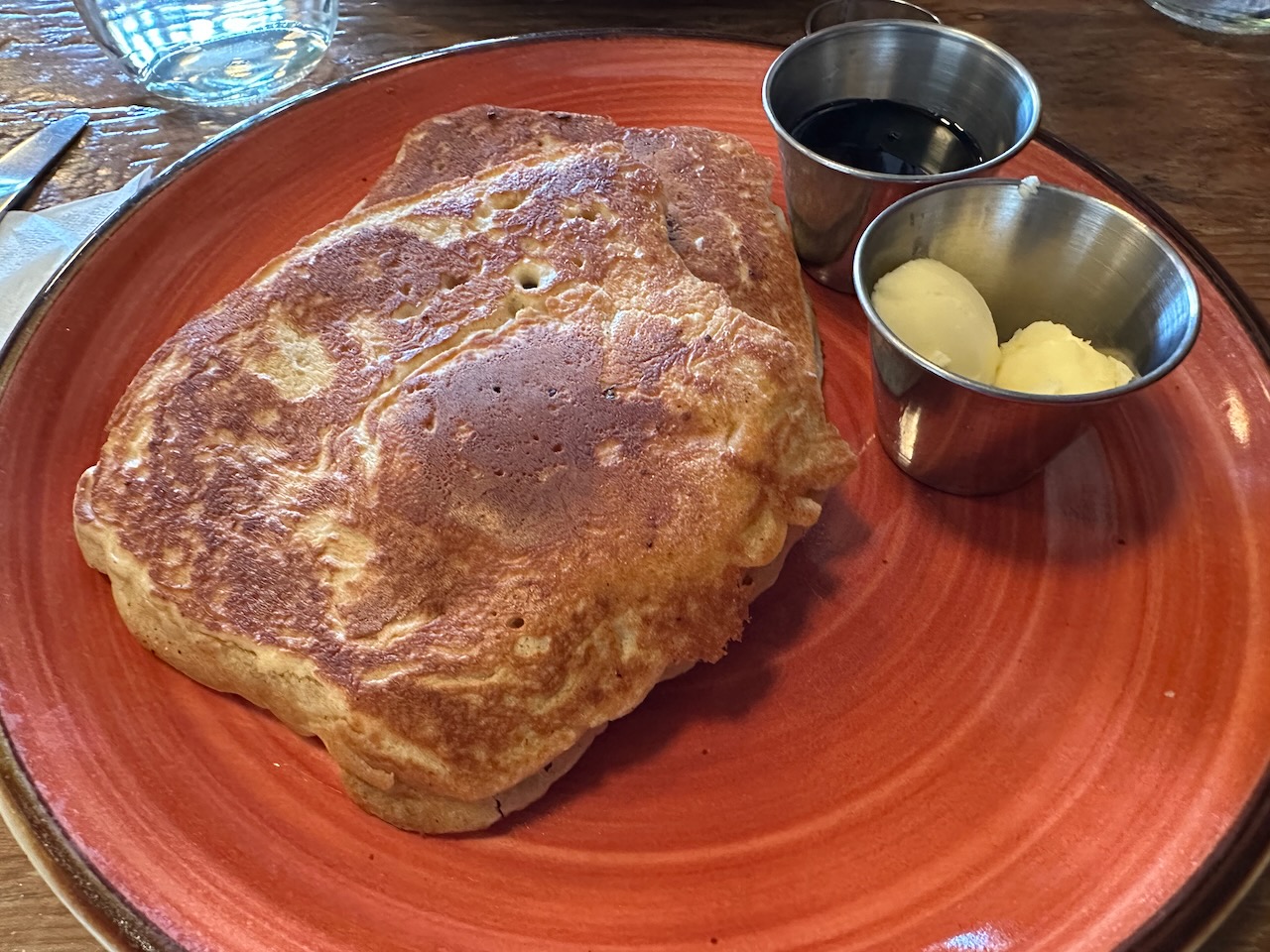 Pancakes on plate, with sides of butter and maple syrup. 