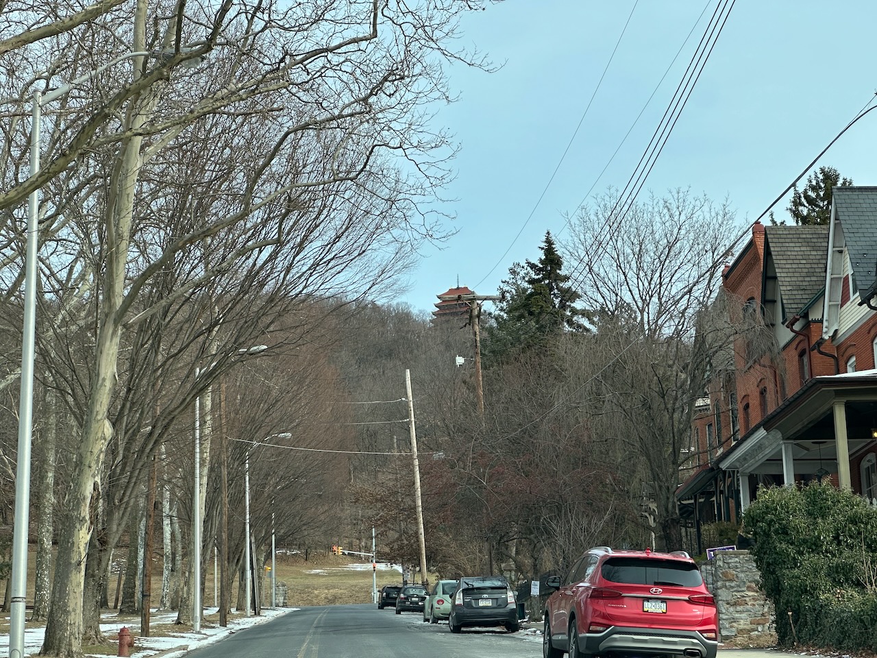 View of street in Reading, with trees along left side of road and houses on right. In the distance the Reading Pagoda is visible atop a hill. 