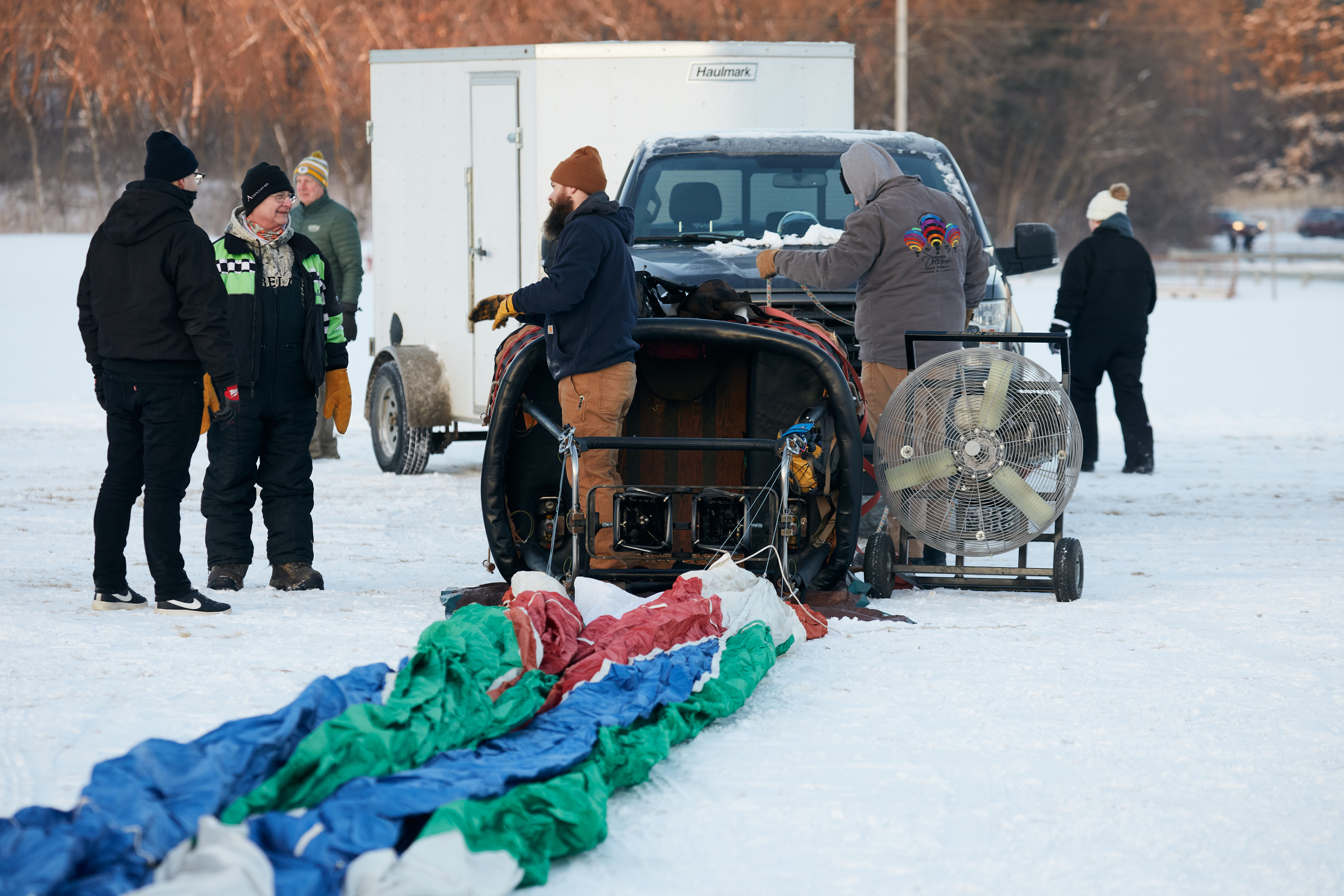 Crew setting up balloon, with basket and ballon laying on side in snow. 