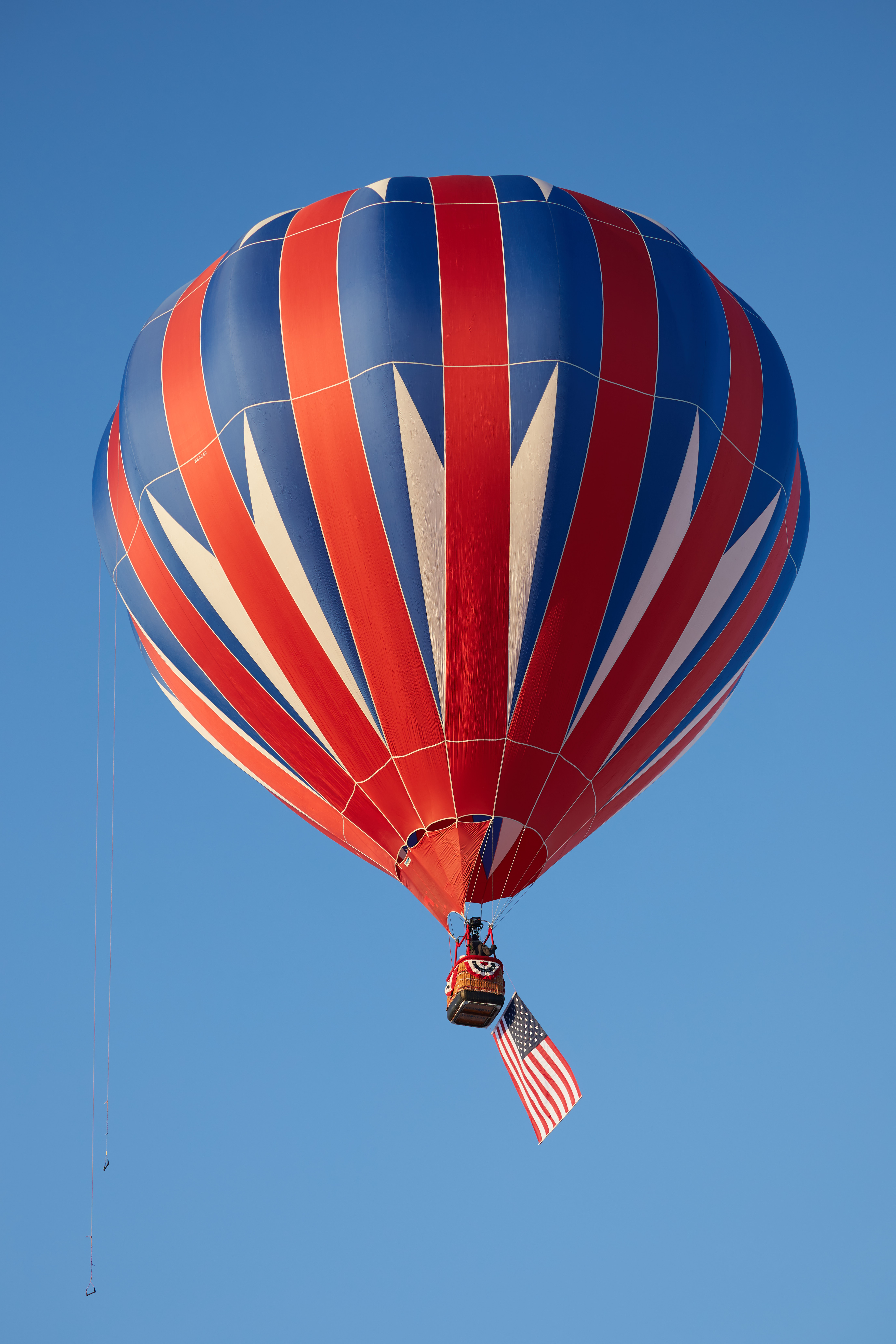 Red, white, and blue balloon in flight, with an American flag flying from basket. 