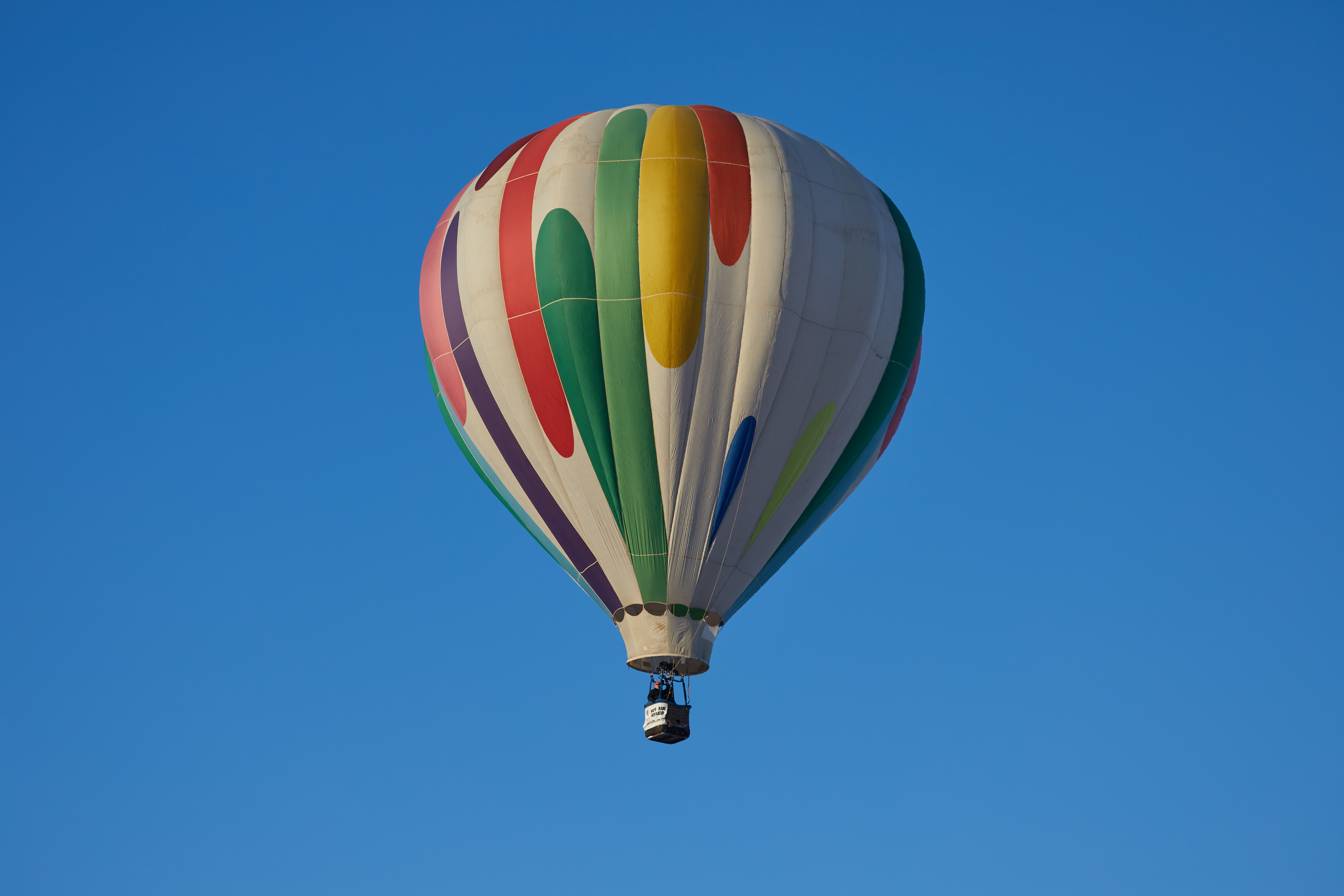 Green, white, orange, and red balloon in flight. 